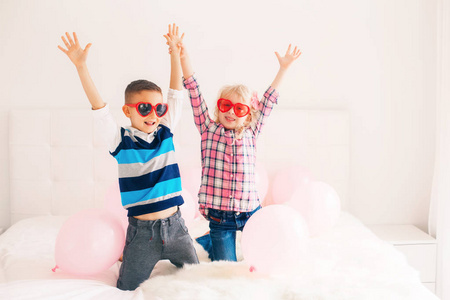 两个快乐的白色白种人可爱可爱的滑稽孩子戴着心形眼镜的团体肖像。 有粉红色气球的男孩和女孩。 热爱友谊和乐趣。 情人节假日庆祝活动