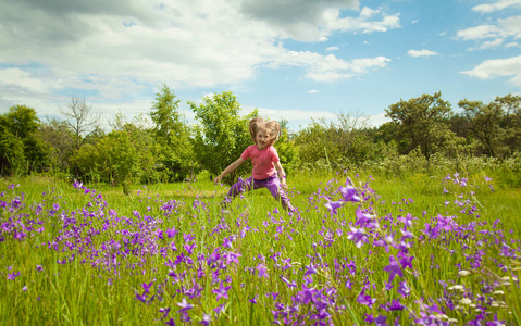 快乐的童年可爱的小女孩在绿色的夏日草地上跳跃