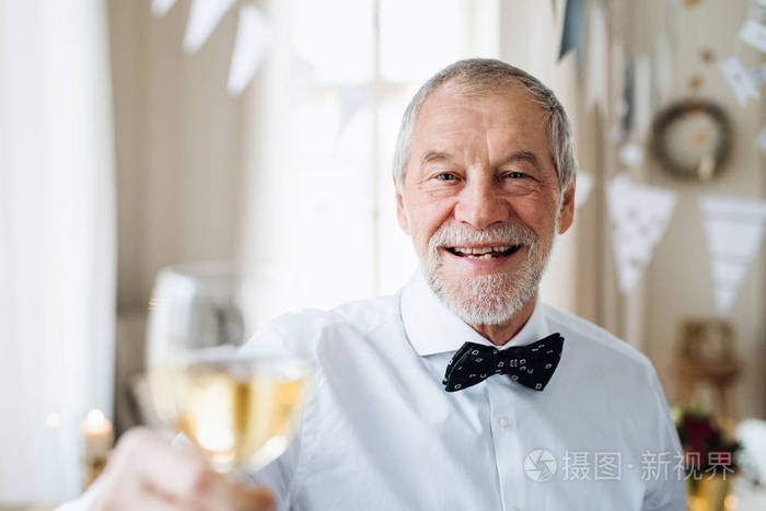 一个老人站在室内参加聚会的房间里拿着酒的画像