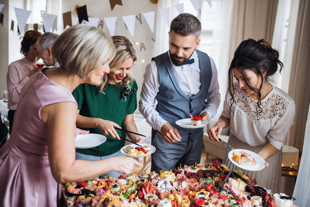 在室内家庭生日聚会上, 多代家庭将食物放在盘子里