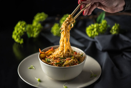 深色背景下,女人用筷子夹着一碗亚洲海鲜面照片