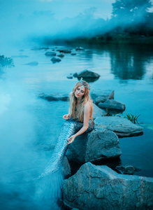金发碧眼的女孩像一个美妙的美人鱼坐在湖中的石头上, 轻轻地, 顺利地