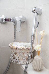 在厕所卫生淋浴，一个篮子里有餐巾纸和花瓶里的人造玫瑰。 现代浴室的马桶