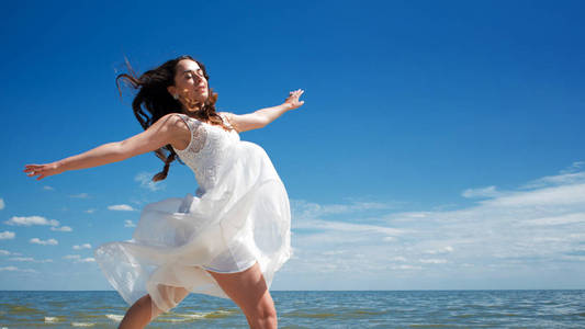 年轻的美丽跳跃的黑发女人在白色礼服
