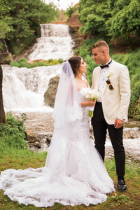 这对幸福美丽的新婚夫妇面对面站在瀑布的背景下