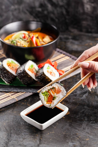亚洲美食的概念。 这个女孩在一家中国或日本餐馆吃寿司，手里拿着木棍。 酱油中的扣篮寿司。 不同的亚洲菜在桌子上