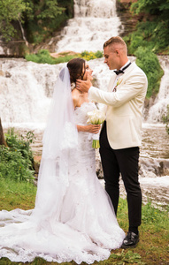 这对相爱的新婚夫妇面对面站在瀑布的背景下