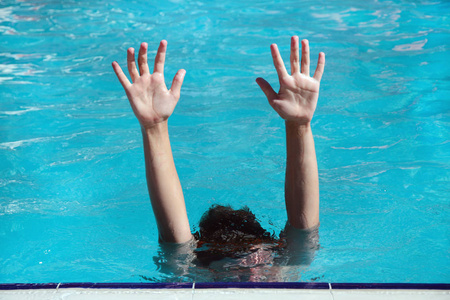 在水下的游泳池里的男孩举起双手在水面上。