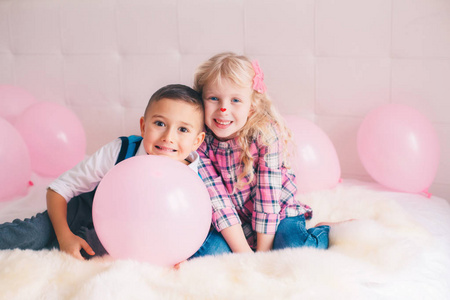 两个快乐的白种人可爱可爱的有趣的孩子坐在卧室的床上的团体肖像。 男孩和女孩玩粉色气球。 热爱友谊和乐趣。 永远是最好的朋友。