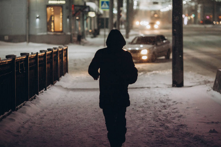 引擎盖雪一个人在引擎盖的剪影, 在晚上走在街上在雪中照片