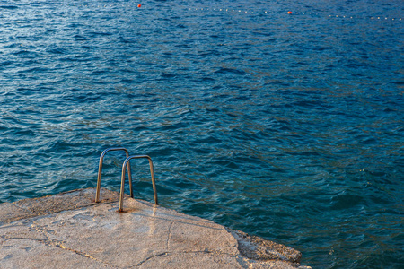 深蓝大海游泳用闪亮的金属扶手。背景上美丽的亚得里亚海海水。在暑假游轮上享受潜水。积极旅游和放松的热门度假胜地