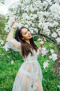 花苹果园里穿着白色礼服的少女画像，看着镜头，触摸着树枝