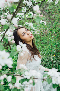 花苹果花园里穿着白色裙子的少女的肖像，看着镜头