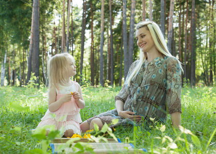 怀孕的年轻母亲和她的小女儿在夏天的公园里度过时光