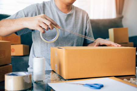 亚洲企业家青少年正在使用胶带密封盒子，通过包装产品发送给客户。