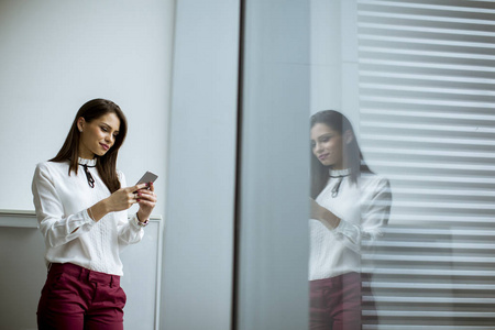 年轻的女商人站在办公室用手机