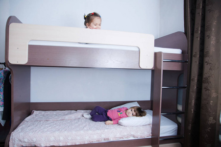 儿童房的双层床。两个小女孩在床上玩。 巧克力阴影在内部与白色墙壁。 儿童家庭用棕色家具