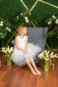 小可爱的女孩，一头金发，穿着白色的连衣裙，绿色的背景上有白花百合花和兰花