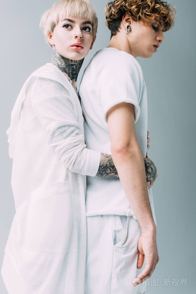 有纹身的迷人女人拥抱英俊的男朋友孤立于灰色