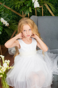 小可爱的女孩，一头金发，穿着白色的连衣裙，绿色的背景上有白花百合花和兰花