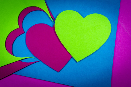 心切出明亮的颜色泡沫片在完整的框架背景下观看。 明亮的绿色和红色的心在蓝色的床单上从上面看。 爱情与关系情人节与色彩趋势概念
