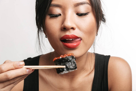 一个快乐的亚洲女人独自坐在白色背景下，用筷子吃寿司