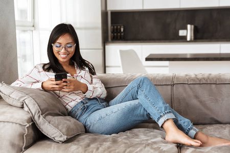 一张20多岁的亚洲美女在舒适的平板沙发上躺着手机的照片