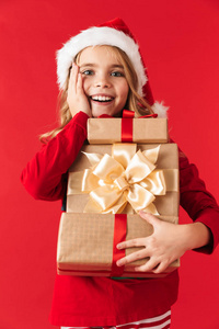 穿着圣诞服装的快乐小女孩站在红色背景下拿着礼品盒