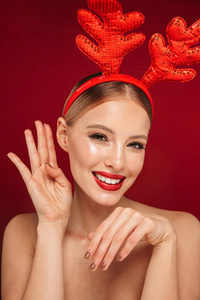 一位年轻的无胸美女的美丽肖像，她身穿圣诞驯鹿角，妆点在红色背景下