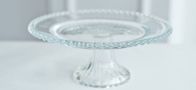 玻璃圆台上装饰着玻璃球，用来做蛋糕和甜点，放在白色背景的白色桌子上。