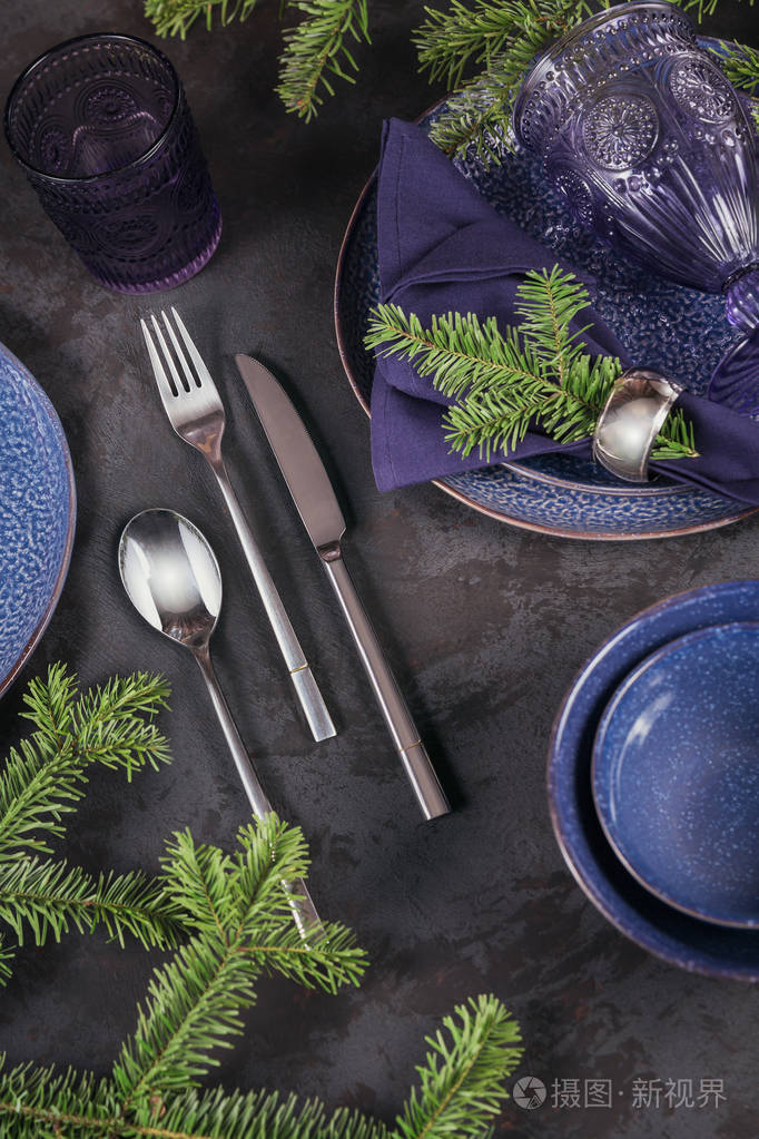 深蓝色装饰与杉树枝. 盘子酒杯和餐具与装饰纺织品在黑暗的背景.