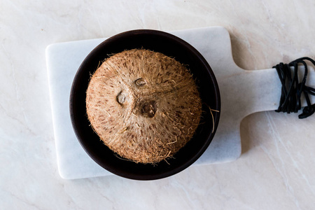 新鲜的有机棕色生椰子在深色的木碗里。 有机食品。