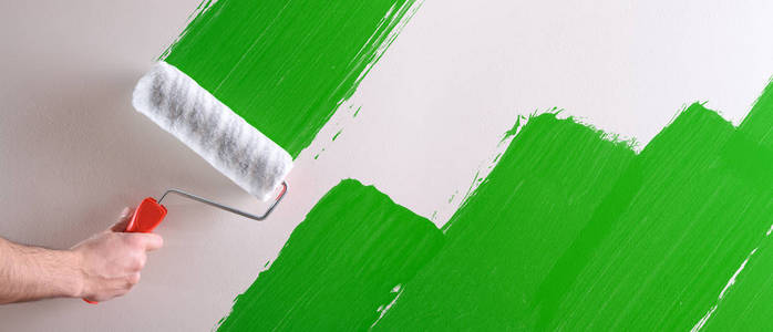 s hand painting a green sample with roller on a white wall. Hori