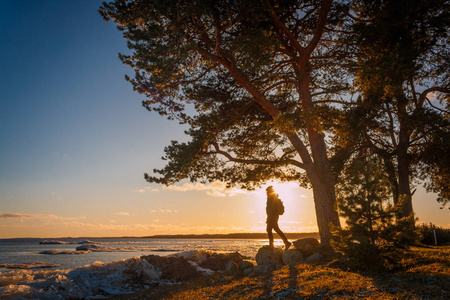 冬天日落时分，在靠近佩普西湖的爱沙尼亚南部，年轻人站在湖岸的树下