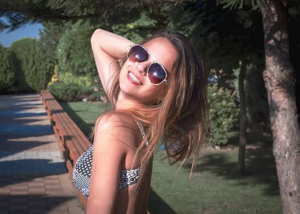 下午，年轻漂亮的女孩戴着太阳镜在公园的背景下晒太阳