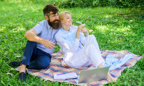 家庭享受放松的自然背景。一对留胡子的男人和金发碧眼的女人坐在绿色的草地上放松自然。双人与笔记本电脑放松自然环境。放松和灵感的概念