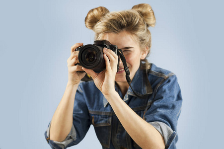 迷人的年轻女人，她的手里拿着一个照片相机，在工作室的一个孤立的蓝色背景。 拍照和录像的概念