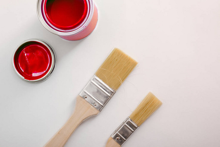 在白色桌子和油漆刷上打开红色丙烯酸油漆罐。 具有文本空间的绘画材料的概念背景。 水平构图。 上面的风景。