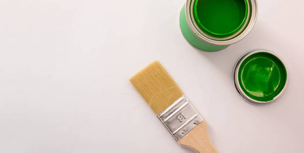 在白色桌子和画笔上打开绿色丙烯酸漆罐。 具有文本空间的绘画材料的概念背景。 水平构图。 上面的风景。