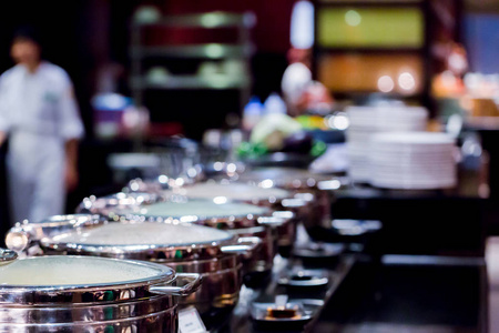 不锈钢锅在自助餐桌上有选择性的焦点。 自助餐桌与一排食品服务蒸锅与模糊厨师。