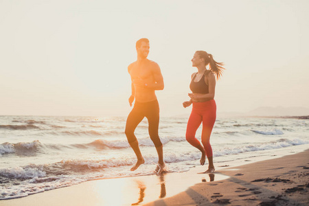 英俊的白种人男人和美丽的女人在日落时在沙滩上奔跑。