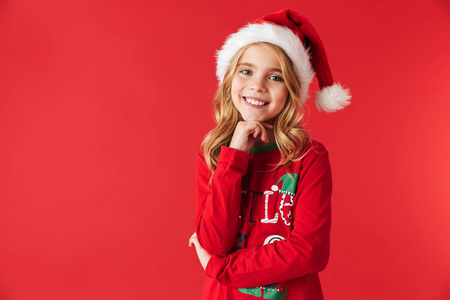 穿着圣诞服装的活泼可爱的小女孩站在红色背景下，看着摄像机