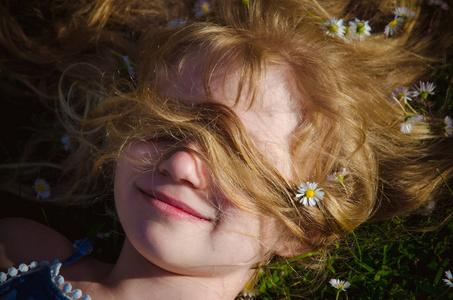 可爱的女孩，长长的金发躺在草地上绿草如茵的雏菊中
