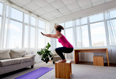 侧视年轻女子在客厅做盒子跳跃运动，在家里复制空间。 跳蹲。 运动健康生活方式概念