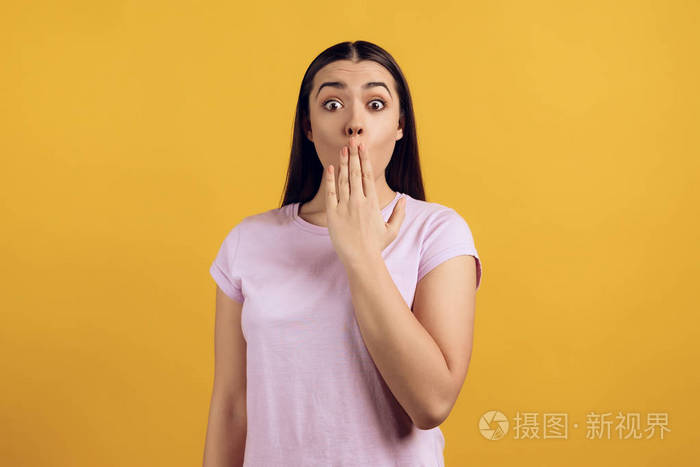 年轻害羞的女孩用手掌捂住嘴孤立在黄色背景上工作室肖像
