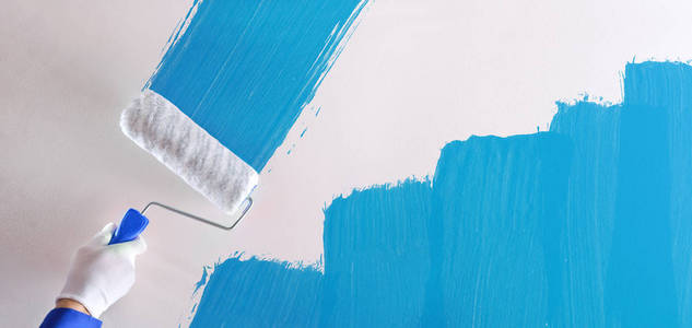 s hand painting a blue sample with roller on a white wall. Horiz