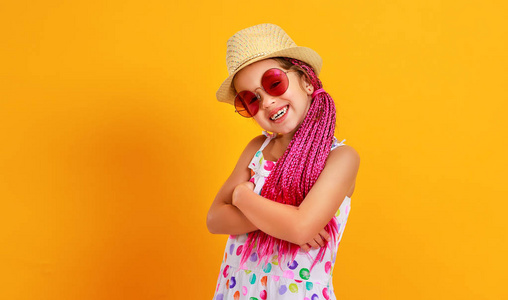 有趣的快乐女孩夏天穿着粉红色的眼镜和帽子笑在彩色黄色的背景上