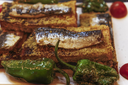 里斯本葡萄牙传统沙丁鱼提供食物。 近距离观看烤沙丁鱼烤面包与橄榄油，青椒和西红柿装饰。