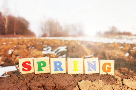 春天，一个由木制立方体组成的五颜六色的铭文矗立在一片犁地上。场工作季节的开始..农工农场业务。雪在地上融化
