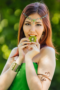 一位穿着绿色连衣裙戴德玛戴着头咬猕猴桃的美丽年轻亚洲女子的肖像。